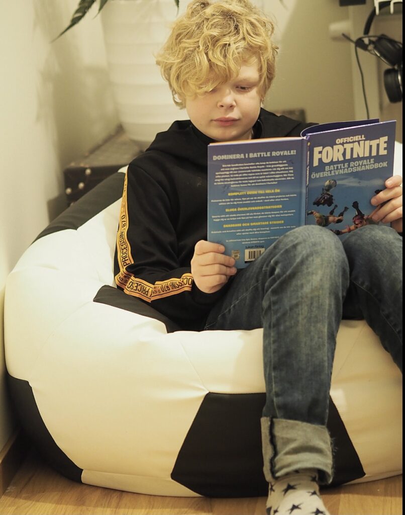 My's son sitter i en fotbollspuff och läser en bok tidning