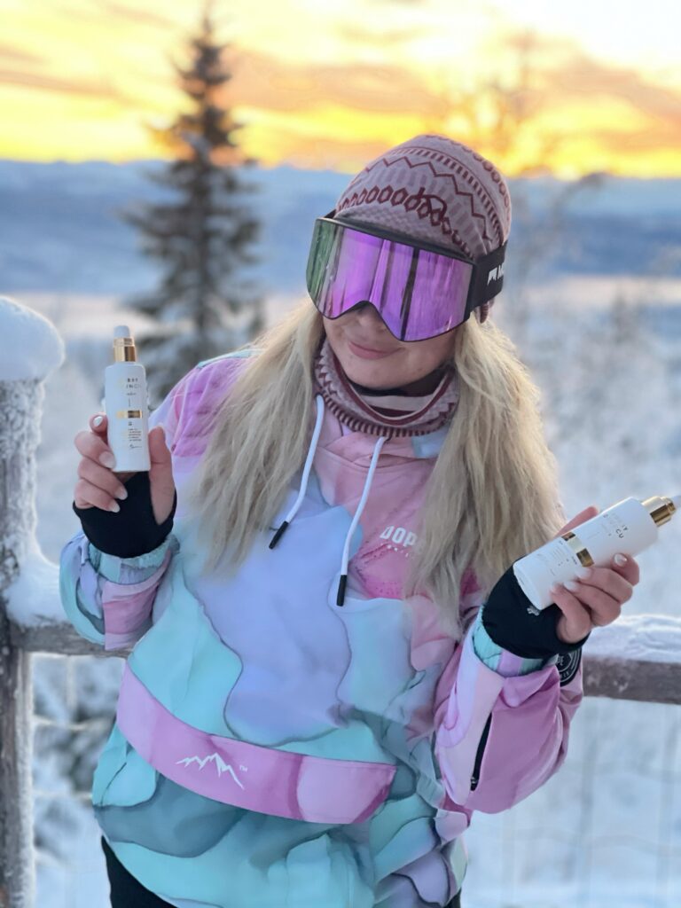En bild på My som håller i Bobby Oduncu Sweden produkter för håret. Hon har på sig en rosa, lila och blå skidjacla, mössa och brillor. Bakom hennes syns ett vinterland med solnedgång.